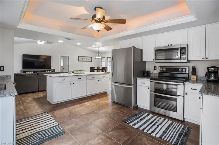 Kitchen with white cabinets, stainless steel appliances, a tray ceiling, and stone countertops