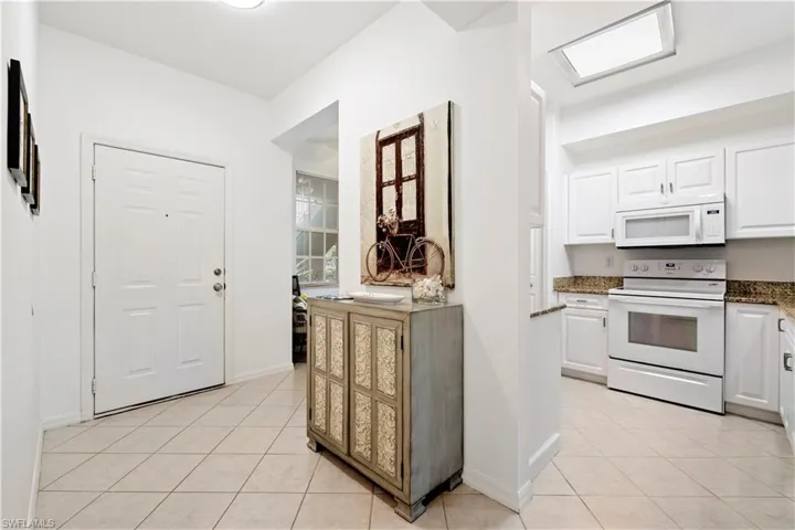 Kitchen with white appliances, white cabinetry, light tile patterned flooring, and dark stone countertops