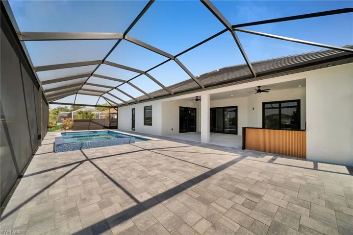 View of swimming pool featuring glass enclosure, a ceiling fan, a pool with connected hot tub, and a patio area