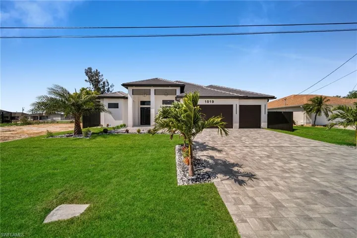 Prairie-style house featuring a tile roof, decorative driveway, an attached garage, stucco siding, and a front lawn