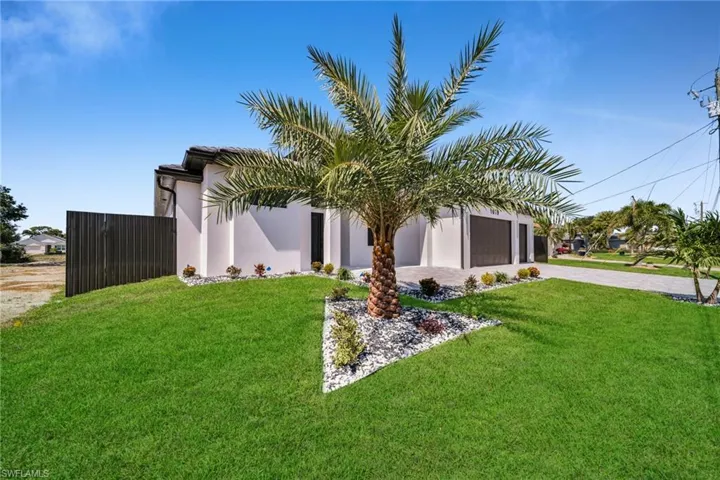 View of front facade with a front lawn, driveway, stucco siding, and fence