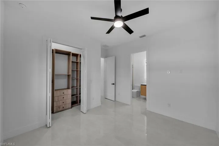 Unfurnished bedroom featuring visible vents, ensuite bathroom, a ceiling fan, and baseboards