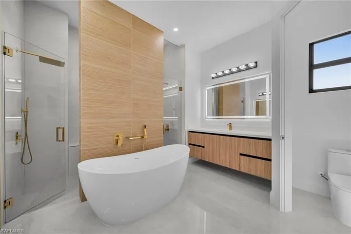 Bathroom featuring a stall shower, toilet, tile walls, a freestanding tub, and vanity