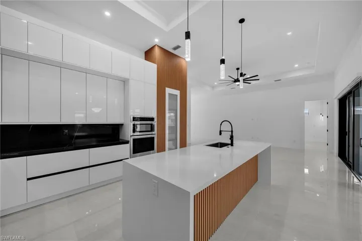 Kitchen featuring stainless steel double oven, a raised ceiling, modern cabinets, and a sink