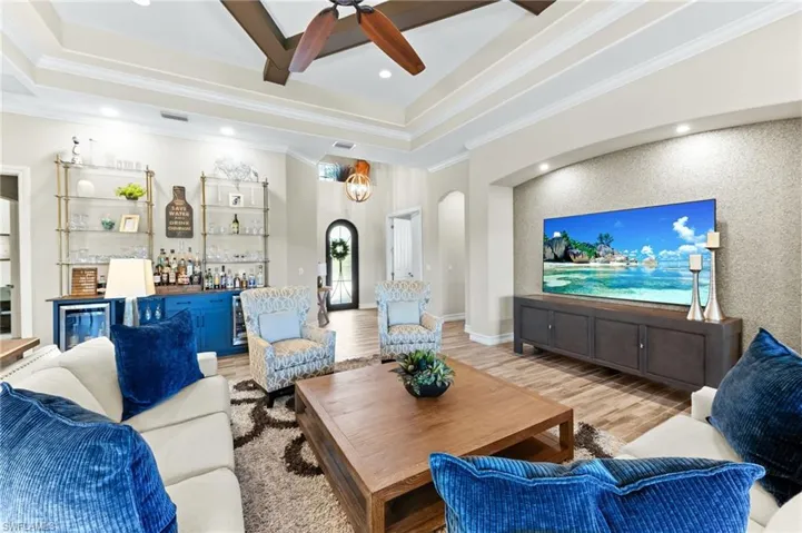 Living room featuring an accent wall, wood finished floors, arched walkways, bar area, and a ceiling fan