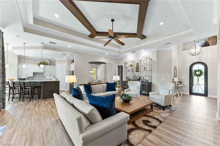 Living area with arched walkways, crown molding, light wood-style floors, beverage cooler, and recessed lighting
