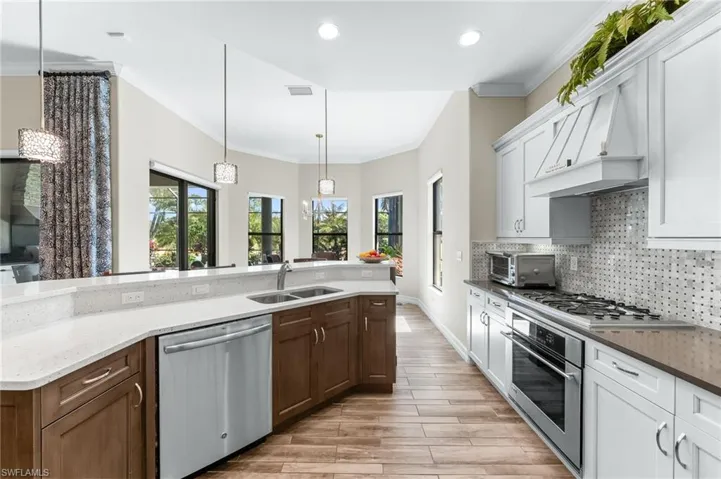 Dual tone kitchen featuring dual tone cabinets, ornamental molding, stainless steel appliances, decorative light fixtures, and dark stone countertops