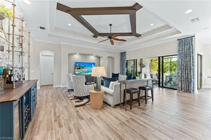 Living room featuring coffered ceiling, arched walkways, ornamental molding, a bar, and recessed lighting