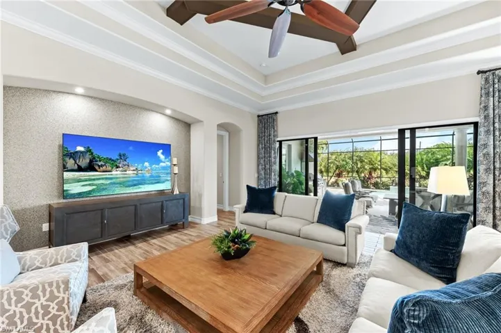Living area with wood finished floors, ornamental molding, ceiling fan, arched walkways, and an accent wall