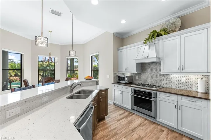 Two tone kitchen featuring two tone color scheme, dark stone counters, stainless steel appliances, ornamental molding, and light wood-type flooring