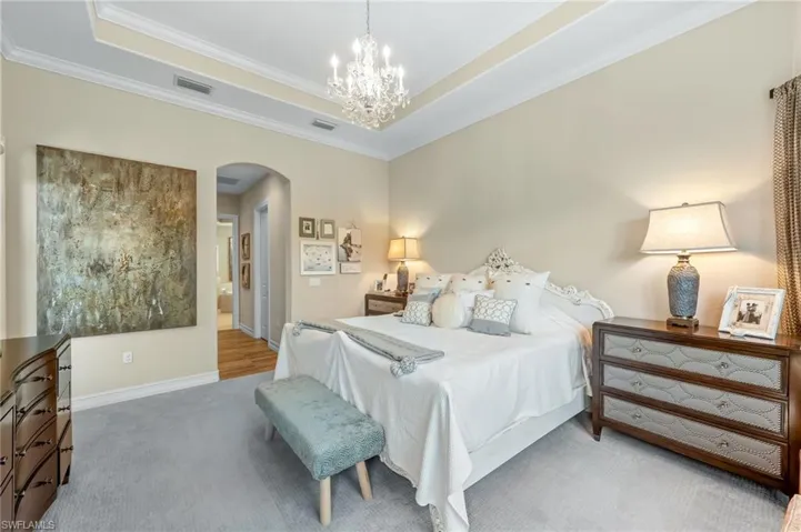 Bedroom with crown molding, a tray ceiling, suspended lighting, carpet floors, and ensuite bath