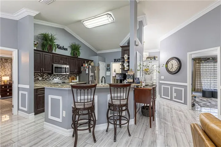Kitchen with light stone countertops, dark brown cabinets, stainless steel appliances, vaulted ceiling, and ornamental molding