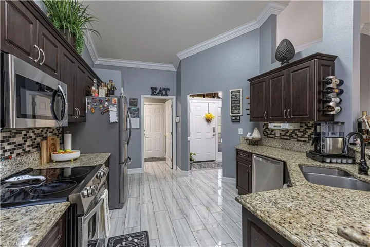 Kitchen featuring dark brown cabinetry, stainless steel appliances, backsplash, crown molding, and sink