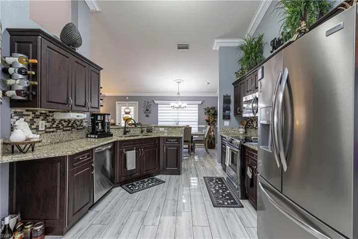 Kitchen with ornamental molding, appliances with stainless steel finishes, light stone counters, sink, and tasteful backsplash