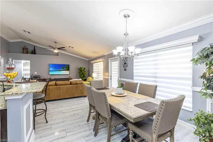 Dining room with ornamental molding, lofted ceiling, light hardwood / wood-style flooring, and ceiling fan with notable chandelier
