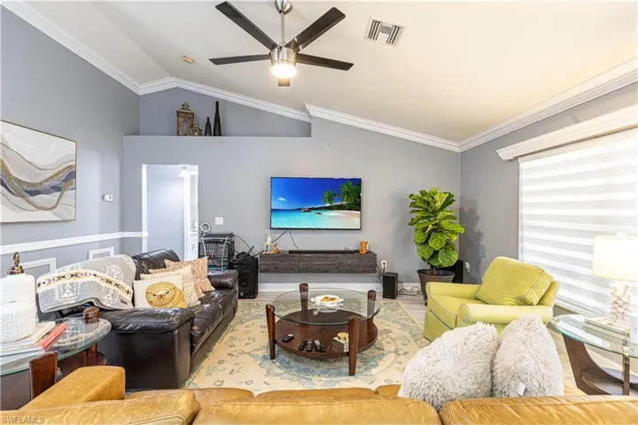 Living room with ornamental molding, ceiling fan, and vaulted ceiling