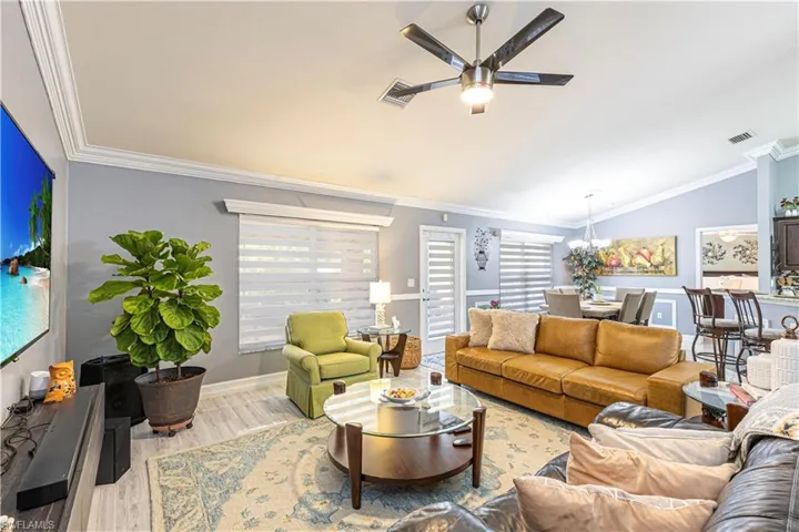 Living room featuring crown molding, ceiling fan with notable chandelier, vaulted ceiling, and light hardwood / wood-style flooring