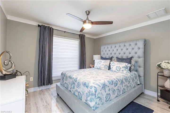 Bedroom with ceiling fan, light wood-type flooring, and ornamental molding