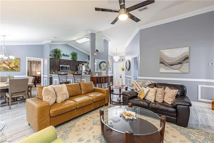 Living room featuring high vaulted ceiling, ornamental molding, light hardwood / wood-style floors, and ceiling fan with notable chandelier