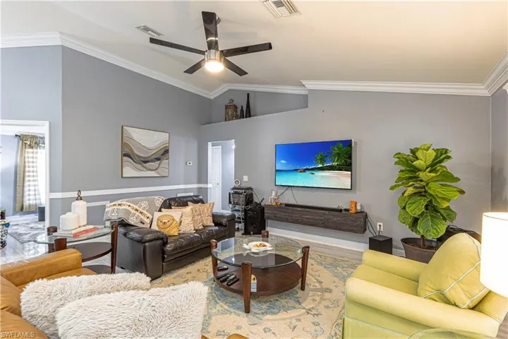 Living room with ornamental molding, wood-type flooring, ceiling fan, and vaulted ceiling