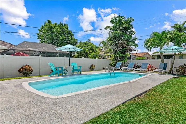 Rectangular in-ground swimming pool with a concrete surround, enclosed by a white privacy fence
