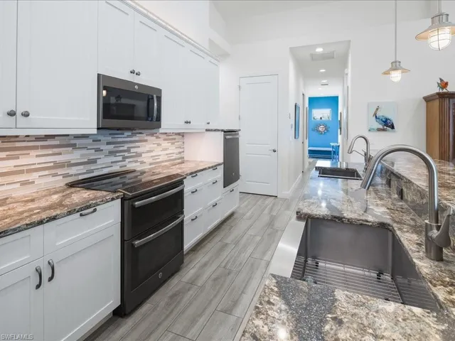 Kitchen with dark stone countertops, double oven range, stainless steel microwave, hanging light fixtures, and wood tiled floors