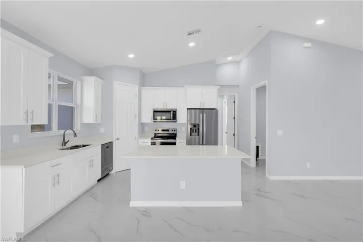 Kitchen featuring lofted ceiling, white cabinetry, a kitchen island, stainless steel appliances, and recessed lighting
