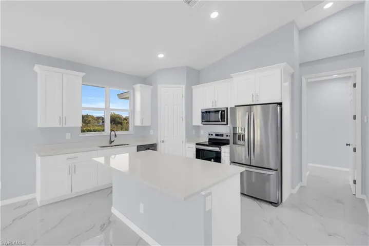 Kitchen with appliances with stainless steel finishes, white cabinetry, a kitchen island, light marble finish flooring, and recessed lighting