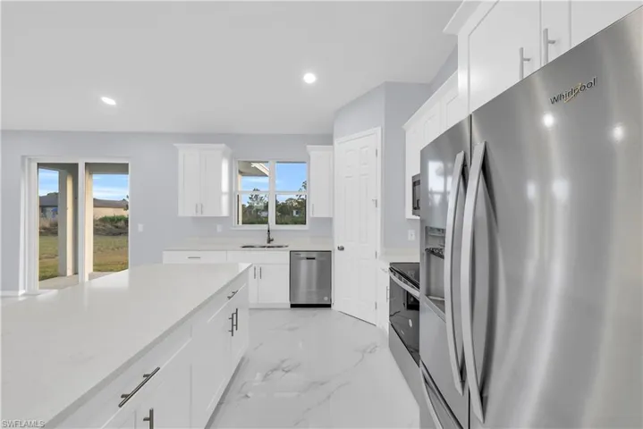 Kitchen featuring appliances with stainless steel finishes, light marble finish flooring, recessed lighting, white cabinetry, and light stone counters