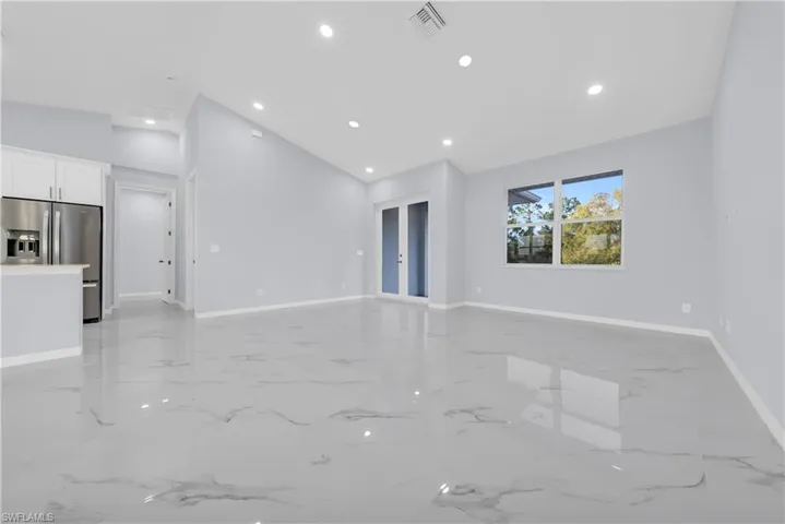 Unfurnished living room with recessed lighting, vaulted ceiling, light marble finish floors, and french doors