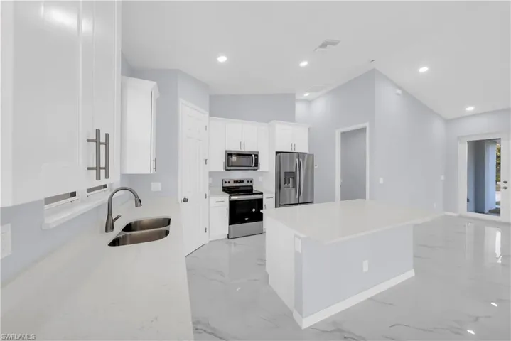 Kitchen featuring stainless steel appliances, light marble finish floors, white cabinetry, light stone counters, and lofted ceiling