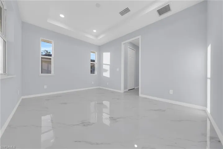 Unfurnished room featuring recessed lighting, a tray ceiling, and light marble finish flooring
