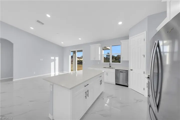 Kitchen featuring appliances with stainless steel finishes, light marble finish floors, a center island, white cabinetry, and recessed lighting