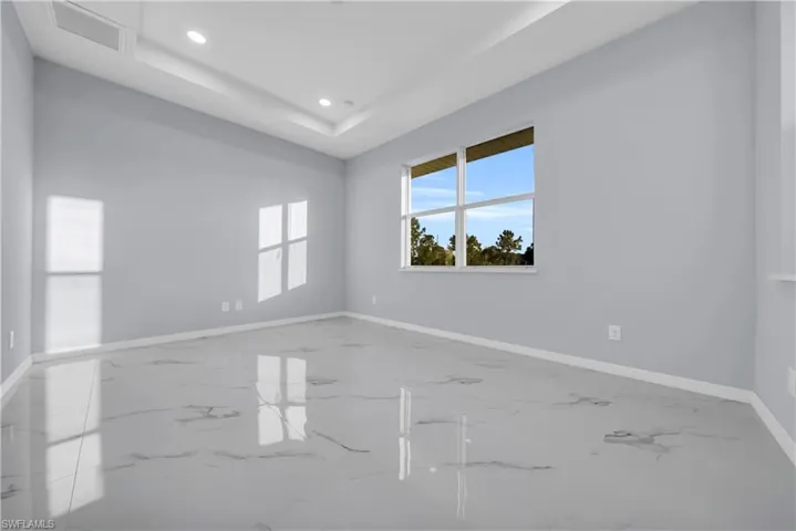 Empty room featuring a raised ceiling, marble tiled flooring, and recessed lighting