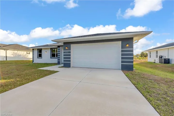 View of front facade with a front yard, stucco siding, concrete driveway, and a garage