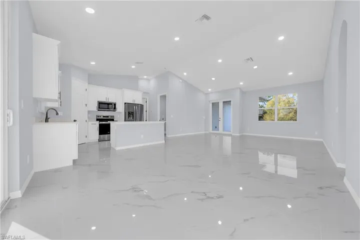 Unfurnished living room with vaulted ceiling, recessed lighting, light marble finish floors, and french doors