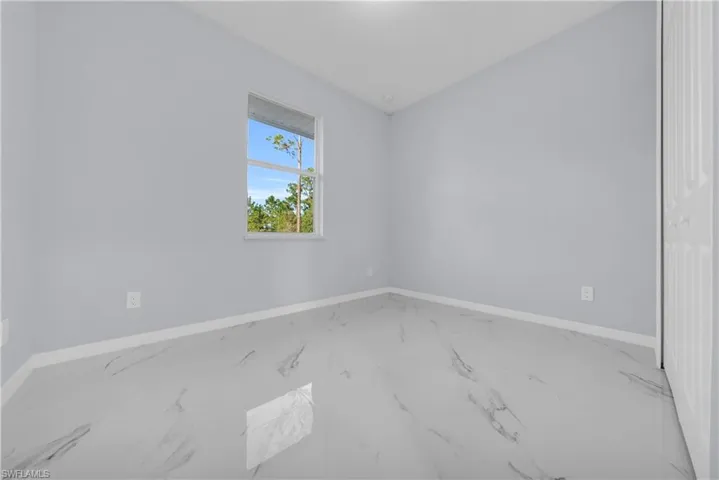 Empty room featuring marble look tiles and baseboards