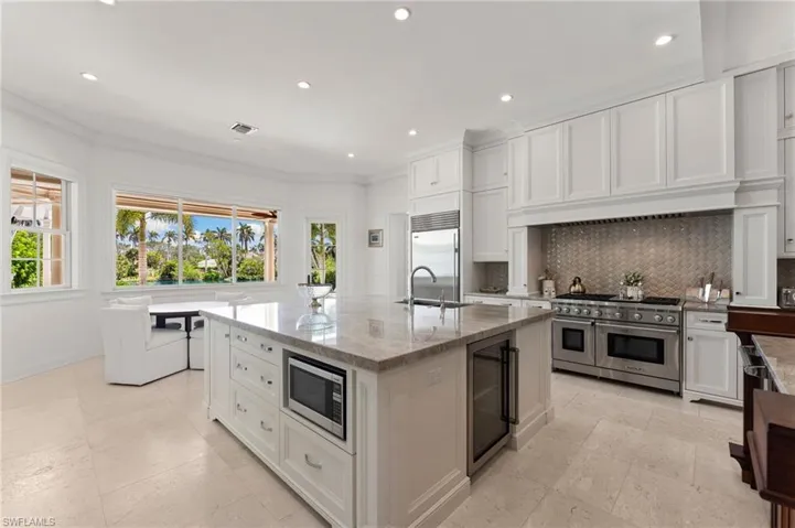 Kitchen featuring built in appliances, a sink, wine cooler, backsplash, and light stone counters