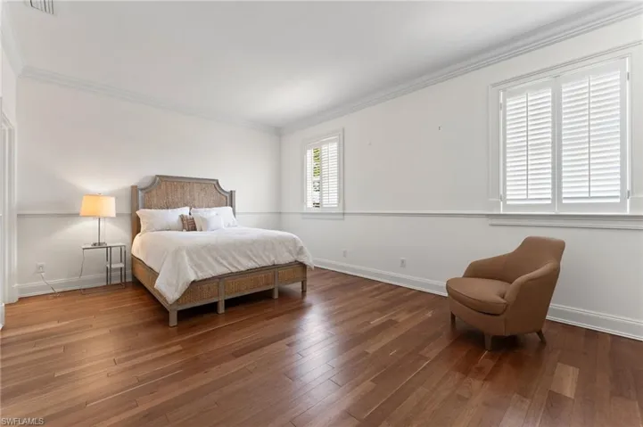 Bedroom featuring wood finished floors, baseboards, ornamental molding, and visible vents