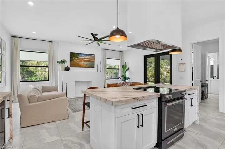 Open-concept living space featuring a kitchen island with integrated range, suspended range hood, and pendant lighting