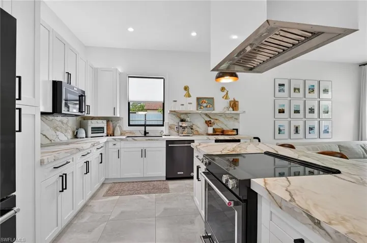 Modern kitchen featuring white cabinetry, integrated black appliances, and veined stone countertops