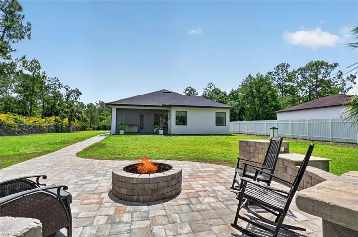 Expansive outdoor living area featuring a stone paver patio, built-in fire pit, and a stone seating wall