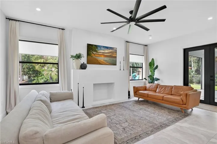 Spacious living area featuring light-toned flooring, a substantial built-in fireplace, and a contemporary ceiling fan