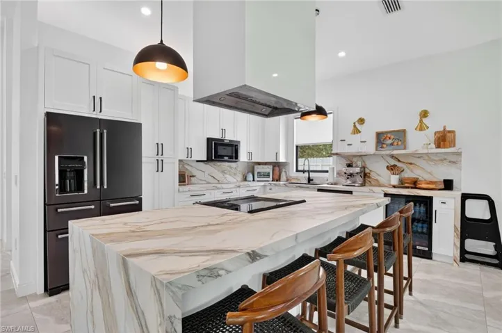 Gourmet kitchen featuring a waterfall island with stone countertop, white cabinetry, integrated black appliances, and a built-in beverage cooler