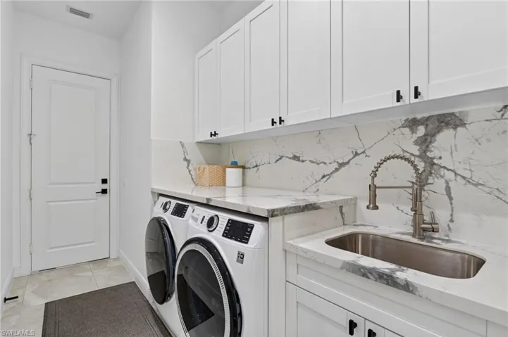 Laundry space featuring white shaker-style cabinetry with matte black hardware, a stainless steel sink with a pull-down faucet, and marble-look countertops with a matching backsplash