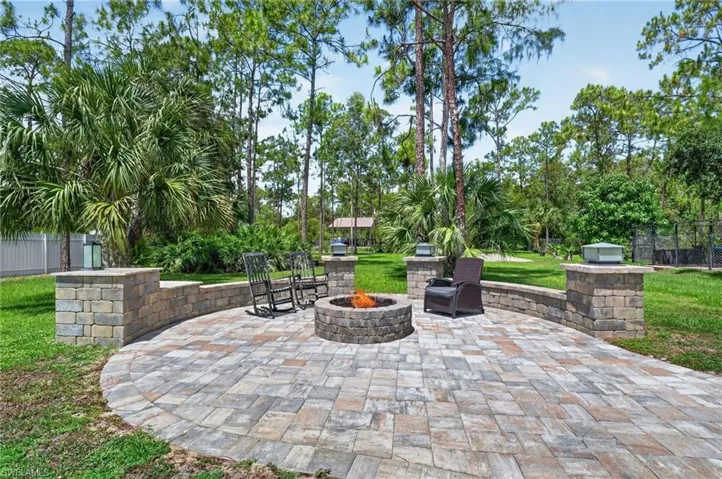 Paver patio featuring a built-in stone fire pit, stone-block retaining wall, and integrated pillar lighting