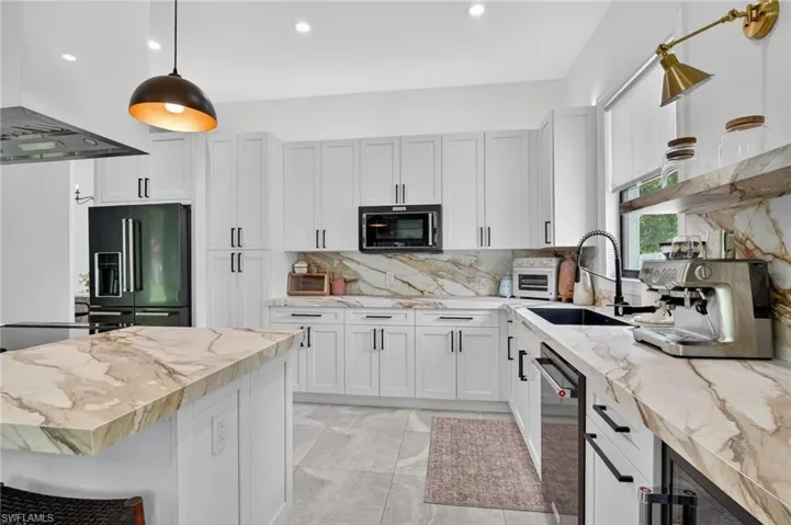 Modern kitchen featuring an expansive island with a waterfall edge, white shaker cabinetry, gold-veined countertops, built-in appliances, and a black sink with a gooseneck faucet