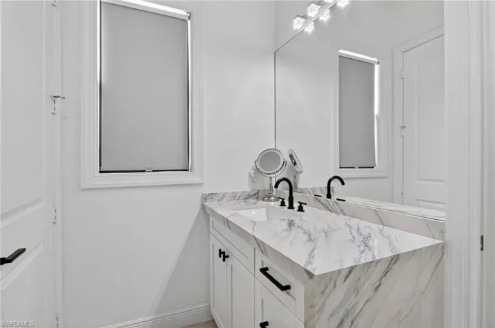 Bathroom vanity featuring a marbled countertop, integrated sinks, white cabinetry, and matte black hardware