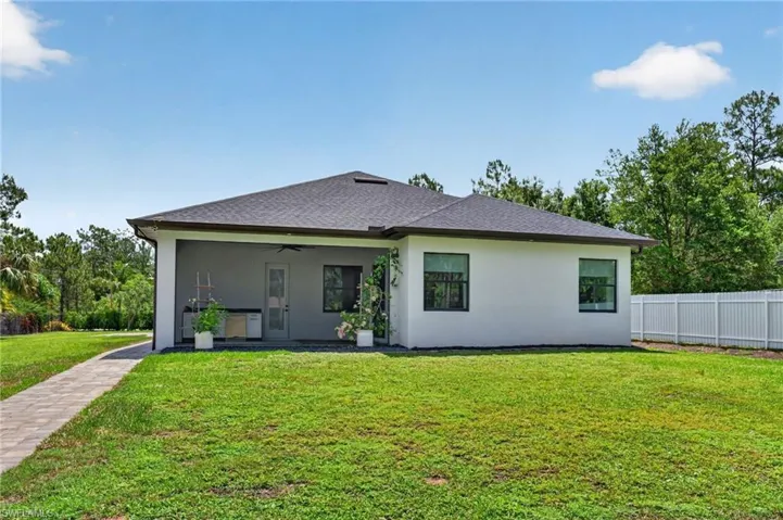 Rear exterior featuring a covered patio, dark shingle roof, white stucco siding, and a paved walkway
