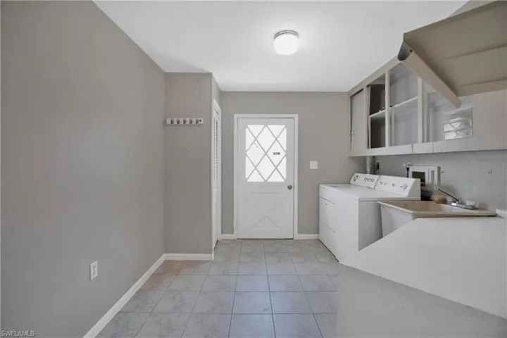 Laundry area with light tile patterned flooring, washer and clothes dryer, and sink